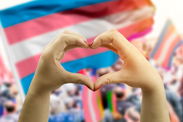 Hands forming a heart in front of a trans pride flag